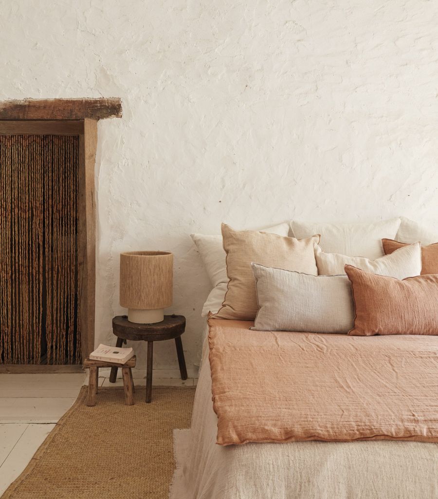 Coussins en lin, lampe en corde et tabouret en bois dans une chambre aux murs chaulés